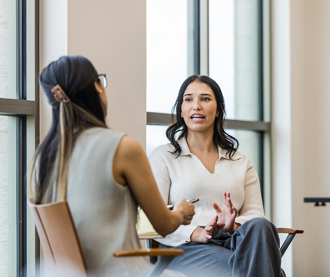 Two employees discussing workplace benefits while seated by a window in an office.