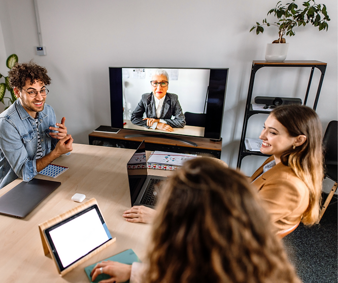 Team in office meeting with remote colleague on video call discussing hybrid engagement strategies