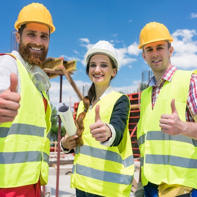 Construction workers in safety gear smiling and giving thumbs up on site for employee efficiency.