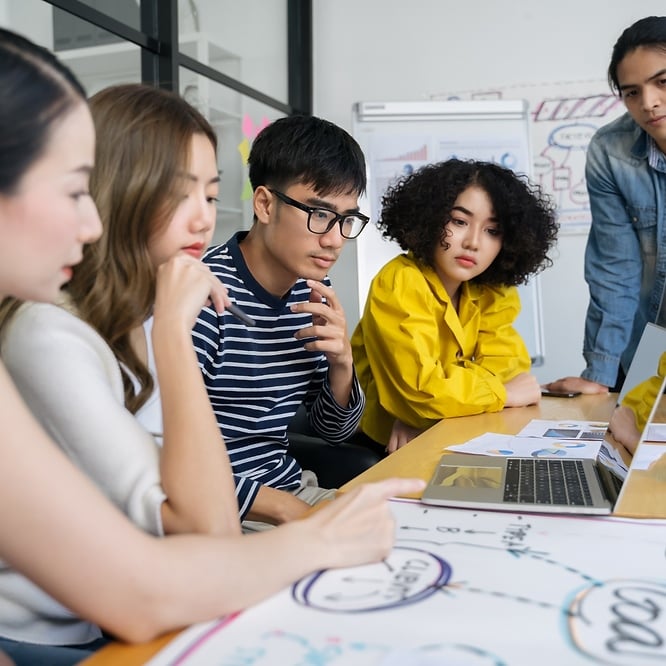 A group of young professionals collaborating around a table with charts and a laptop.